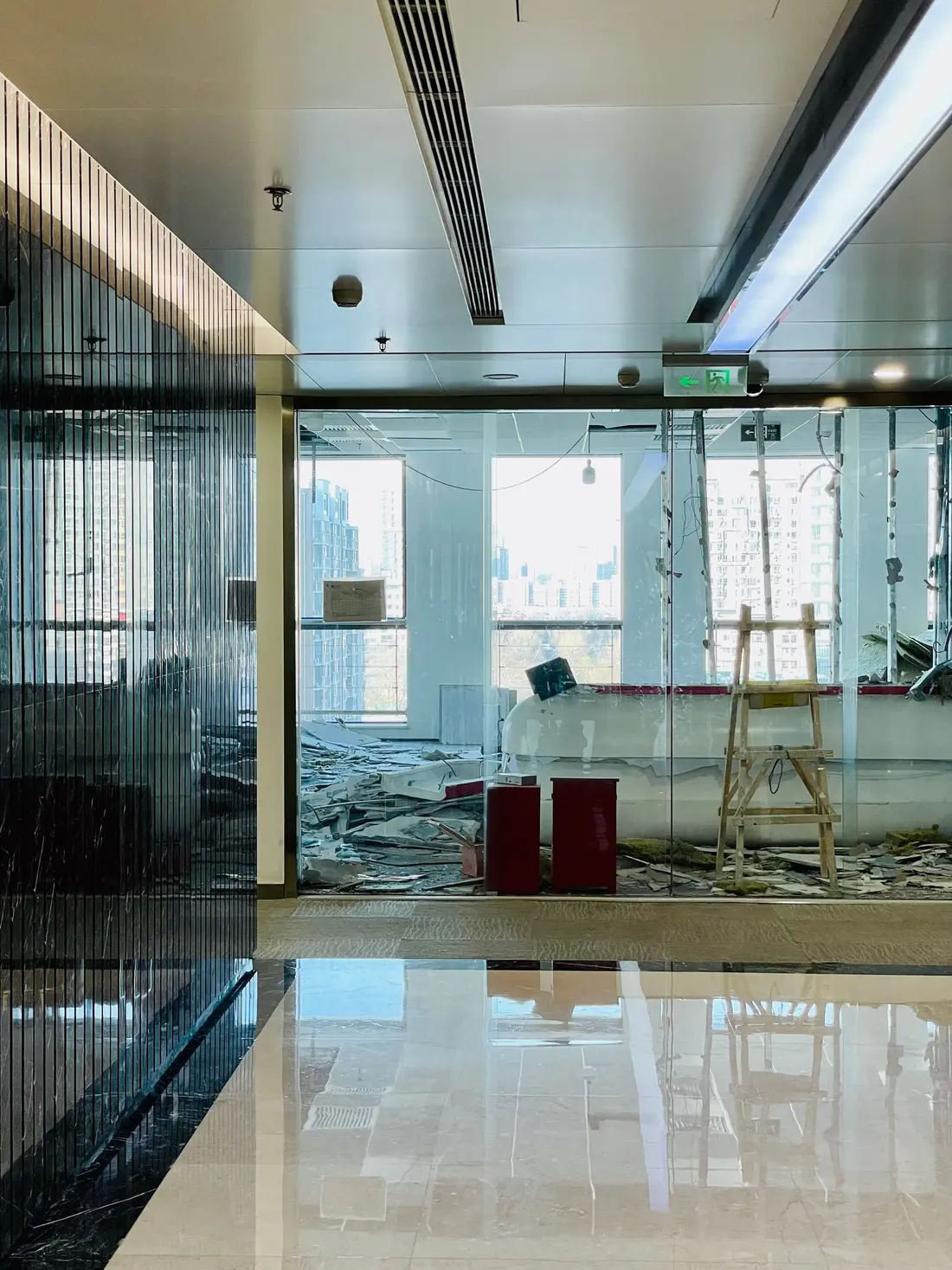 Commercial office interior mid-refurbishment with ceiling debris on the floor behind glass partitions