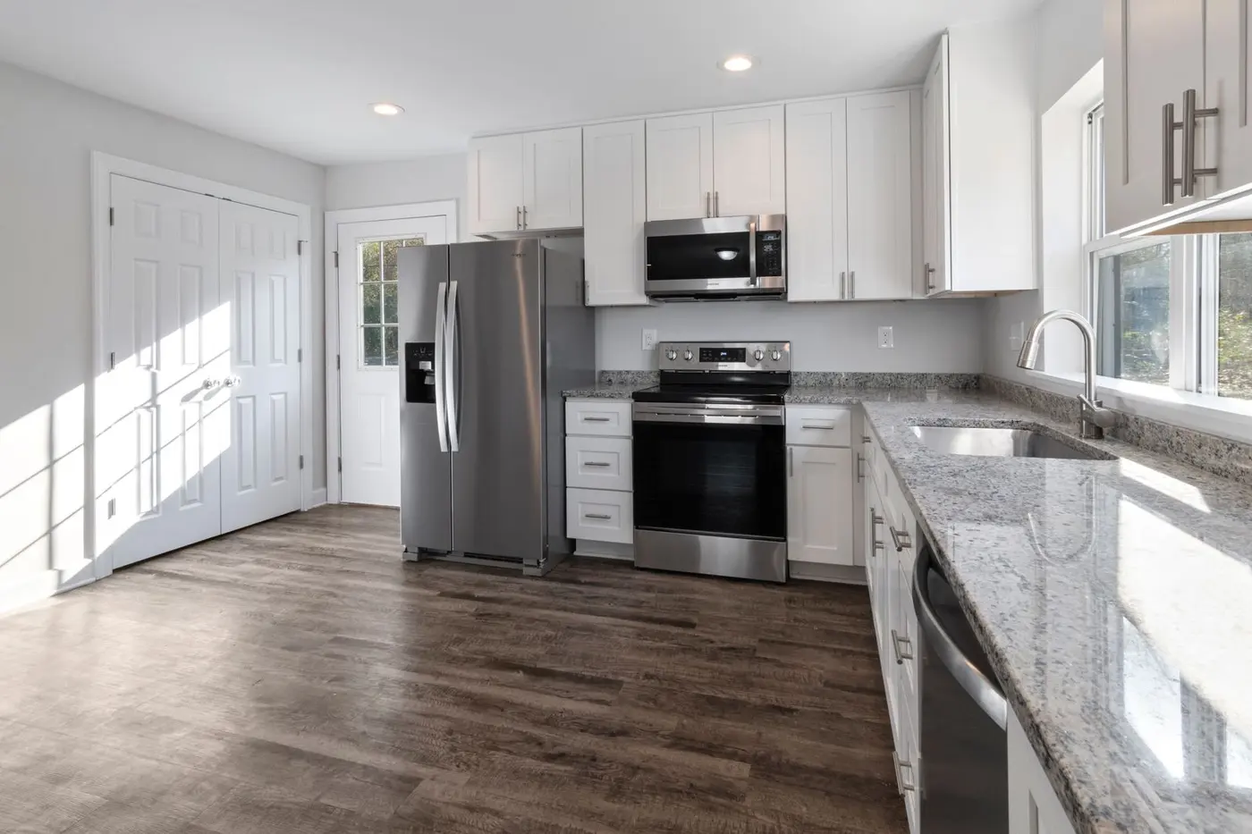 Newly completed kitchen with white cabinetry, granite countertops, stainless appliances and new plank flooring
