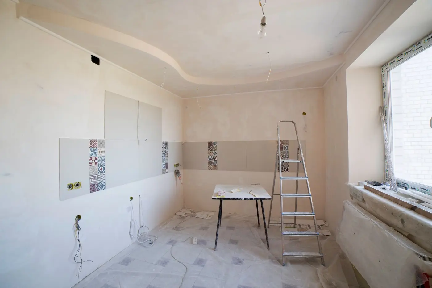 Room mid-renovation with new tiling, protective floor sheeting, a step ladder and exposed wiring