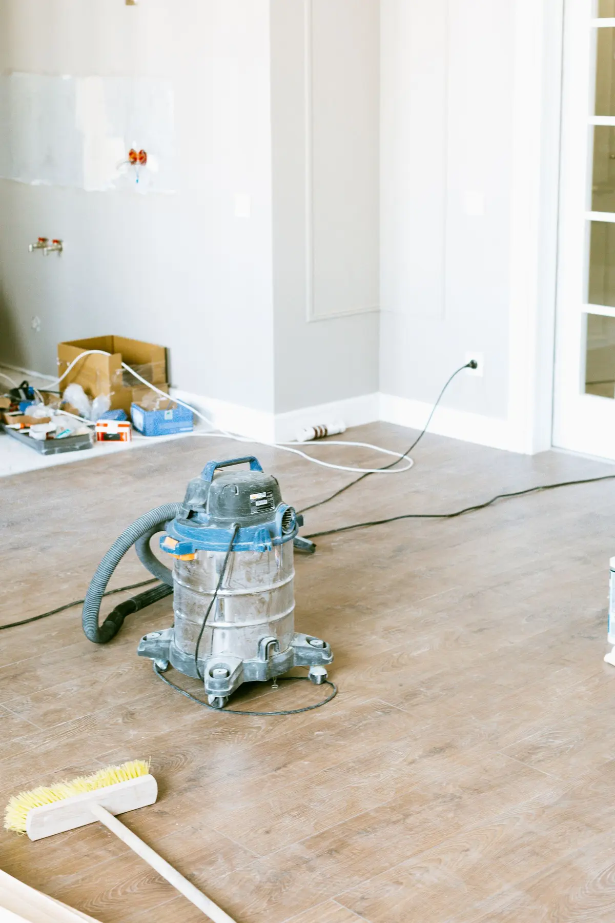 Vacuum and broom on newly installed flooring in a home at the end of a renovation