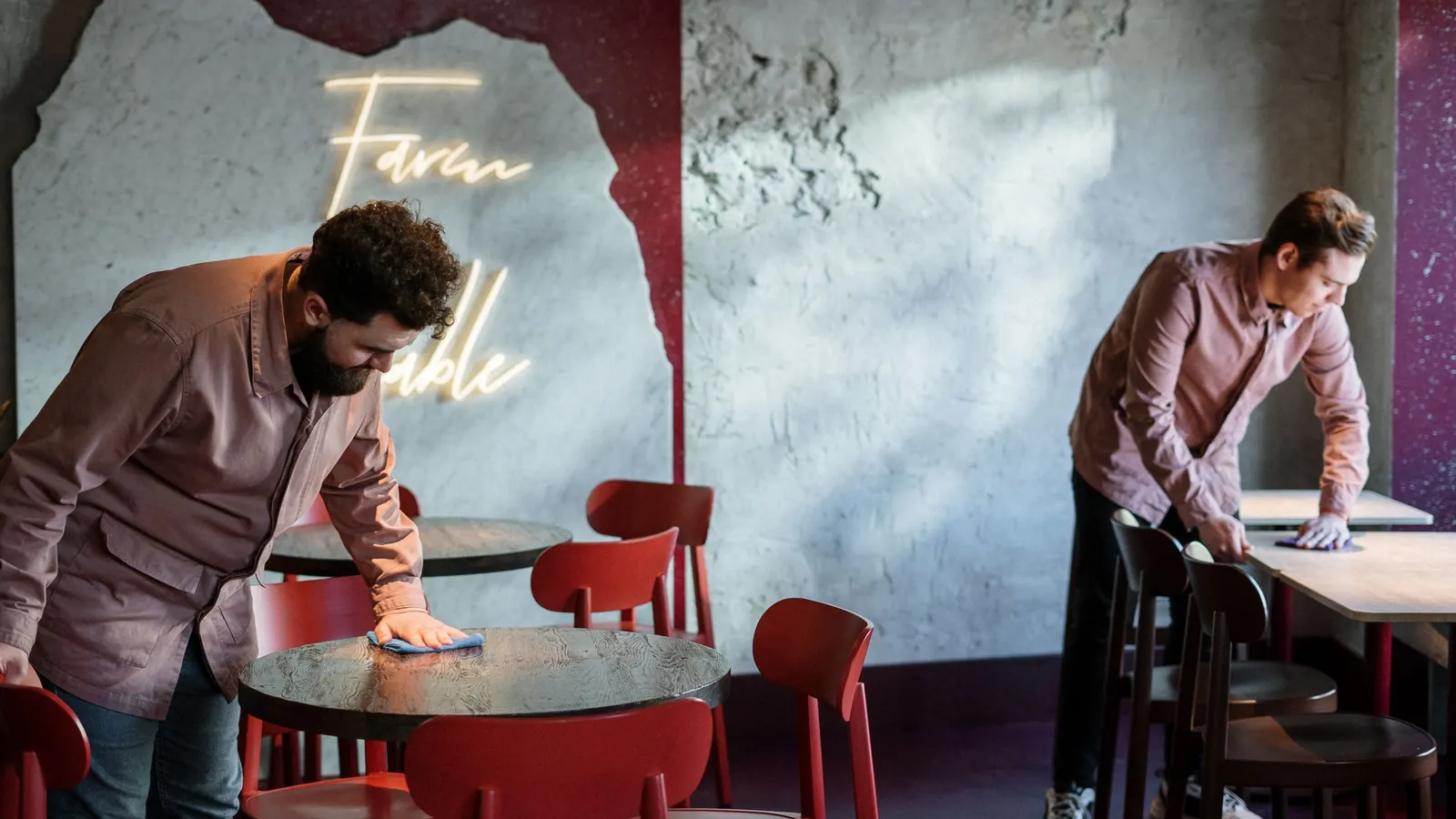 Cleaning staff wiping tables and seating in a closed restaurant dining area