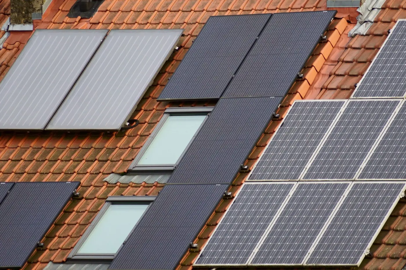 Rooftop solar panels installed across a tiled roof beside skylights