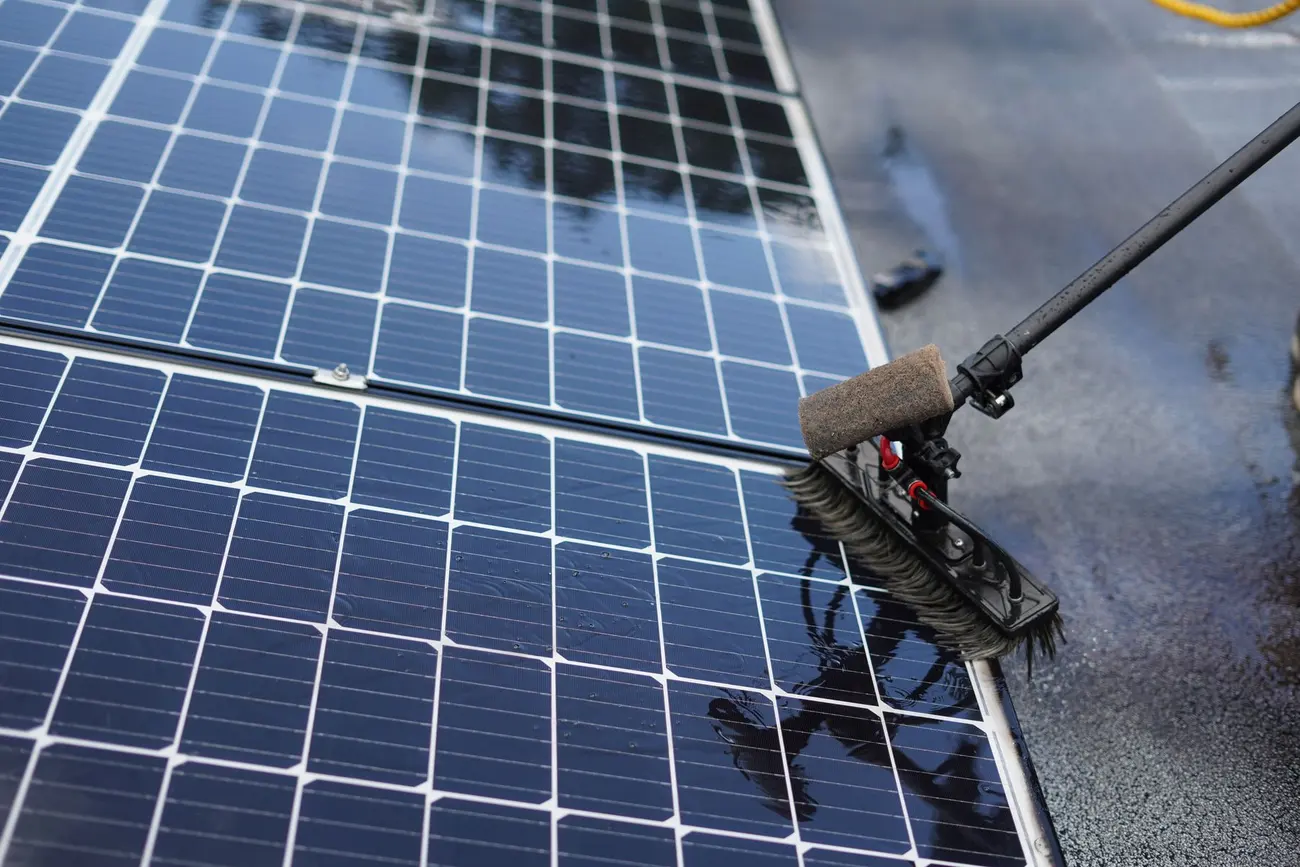 A soft brush head being worked across wet solar panel glass during cleaning