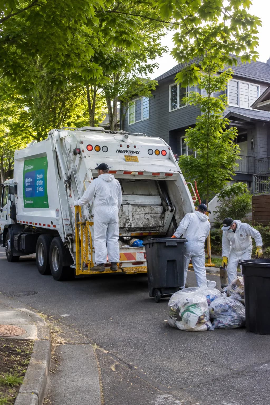 Crew in protective coveralls loading bagged and binned material into the back of a hauling truck on a residential Seattle street