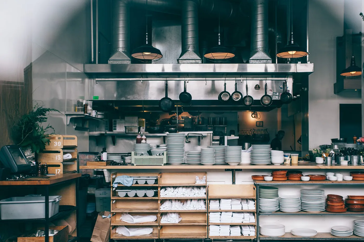 Back-of-house kitchen area with stainless-steel shelving, stacked plates and folded linen