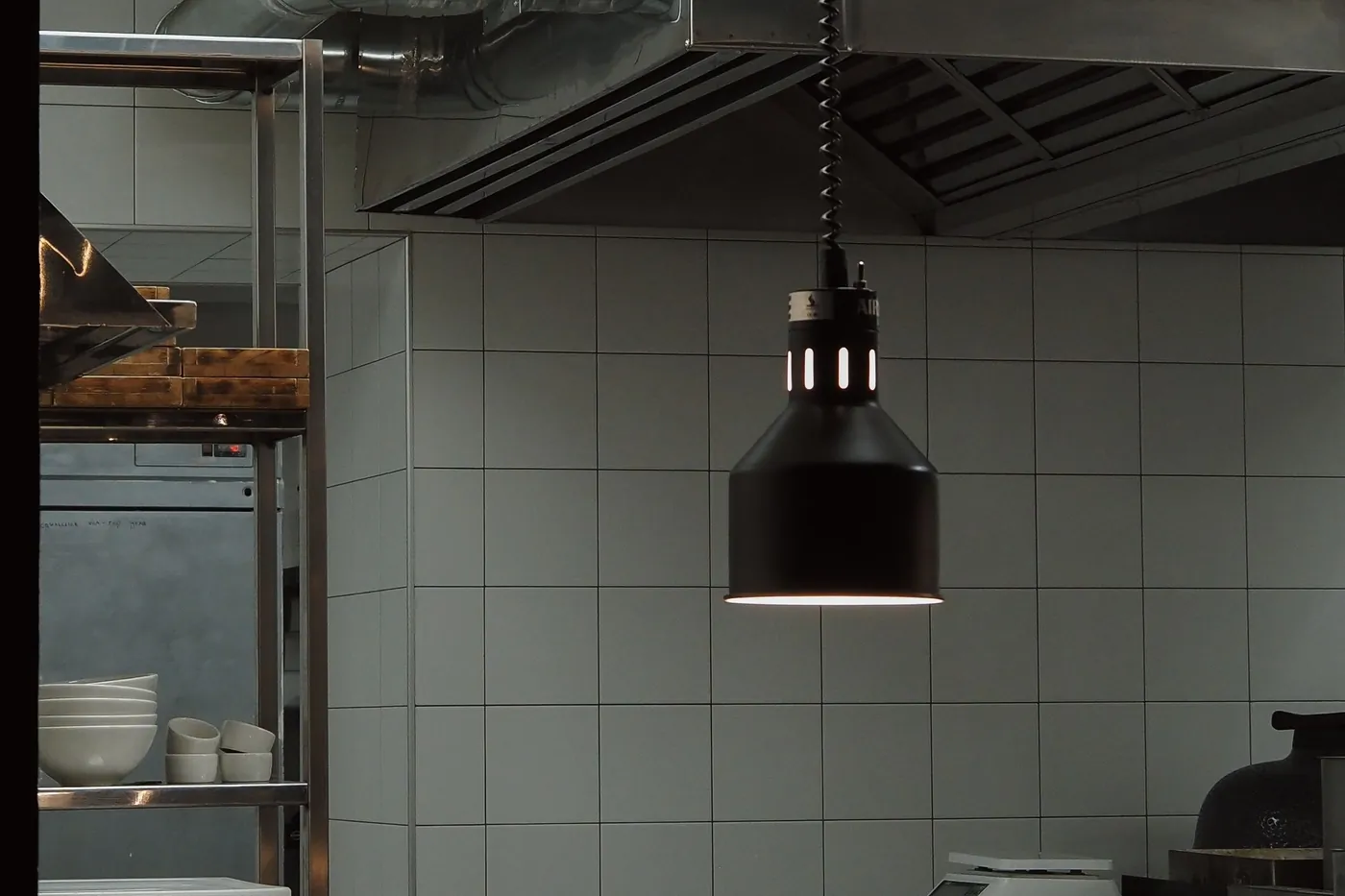 Commercial kitchen work area with ductwork, a tiled wall and stainless-steel prep surfaces